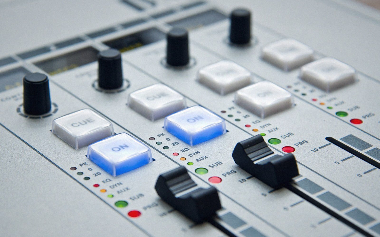 Close-up of an audio mixing console with illuminated blue "on" buttons and sliding faders